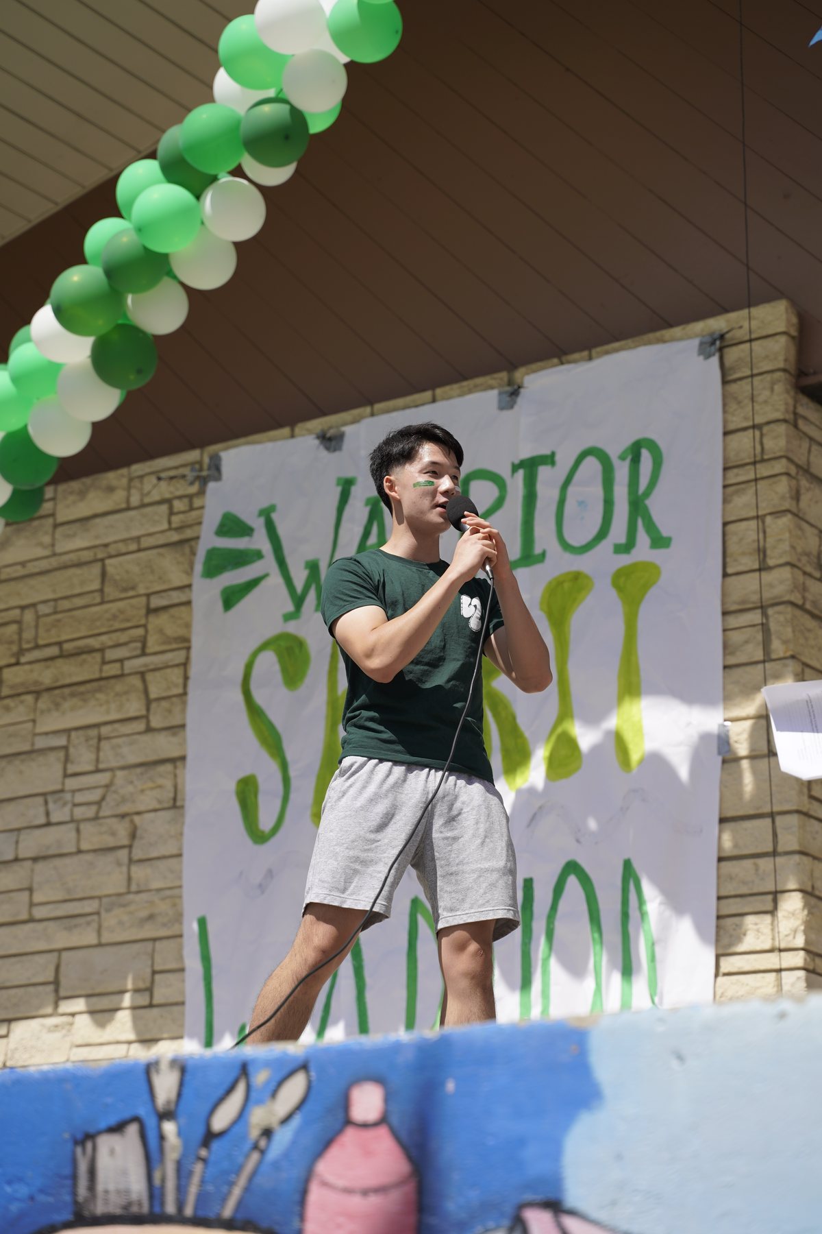 Jadon on the mic at the Green & White Assembly in front of the Warrior Spirit mural